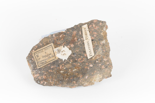 A solid, dark grey mineral specimen with pale terracotta coloured inclusions