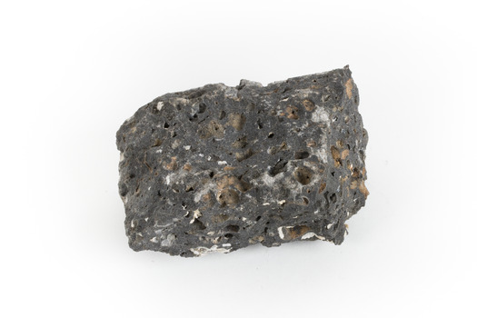 A smaller than hand sized rock specimen which is dark grey in colour with small holes and white deposits across its surface.