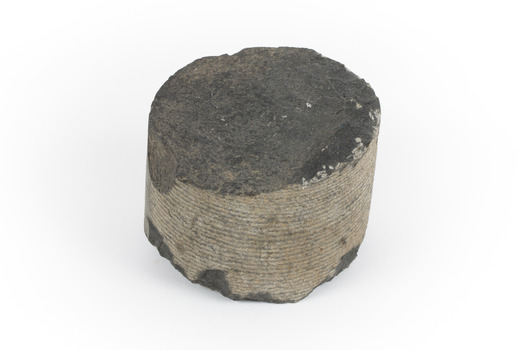 A small cylinder shaped piece of Basalt with smooth sides and broken top and bottom edges.