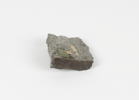 A disfigured rectangular like shape of fine-grained, poorly foliated, porphyroblastic metamorphic rock. The spotted slate is light grey in colour with darker flecks throughout.