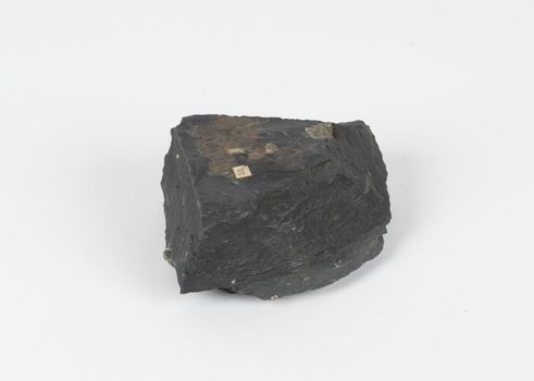 A dark coloured geological specimen with some brown and blue colouration. The shape is roughly triangular, featuring some straight edges and overall geometric shape. The number 53 is adhered to the top surface, a reference to the original catalogue