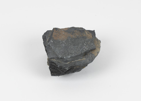 A dark coloured geological specimen with some brown and blue colouration. The shape is roughly triangular, featuring some straight edges and overall geometric shape. 