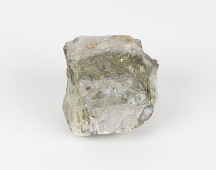 A small round geological specimen with some jagged and hard edges. The colouring is white with dark veins and some gold-like deposits. There is an existing label with the number 104.