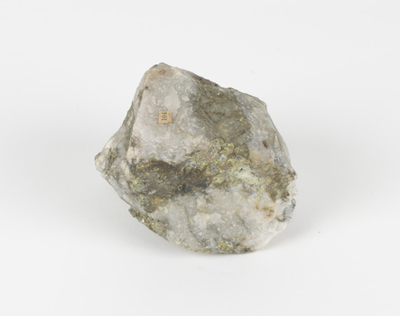 A small round geological specimen with some jagged and hard edges. The colouring is white with dark veins and some gold-like deposits. There is an existing label with the number 104.
