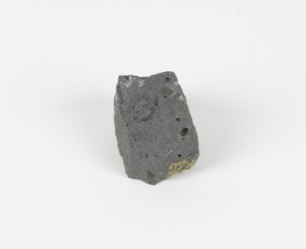 An angular, hand sized grey geological specimen in white spotted grey colours, with one flat brown side.