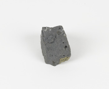An angular, hand sized grey geological specimen in white spotted grey colours, with one flat brown side.
