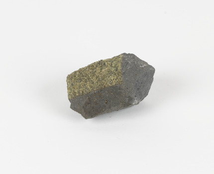 An angular, hand sized grey geological specimen in white spotted grey colours, with one flat brown side.