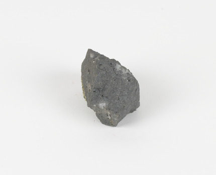 An angular, hand sized grey geological specimen in white spotted grey colours, with one flat brown side.