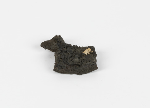 A flat, rough surfaced, irregular shaped, dark grey brown geological specimen with a weathered identification tag attached to the surface and the number 13 written on it.