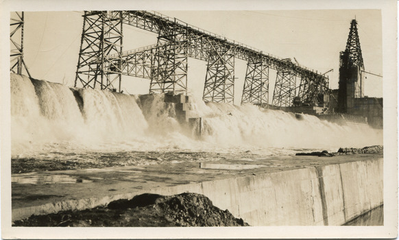 Water rushing down a dam embankment with scaffolding on running along behind the water on the top of the embankment