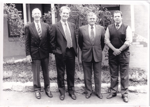 Four men dressed in formal attire standing in front a  period building.