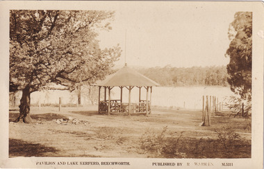 Sepia photograph of a wooden pavilion by a large lake. On the left hand side of the photograph is a large image. On the right hand side there is a broken fence.