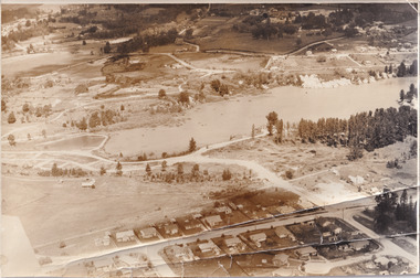 Black and white aerial photograph of a lake with surrounding landscape and township.