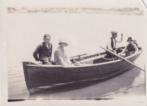 Black and white photograph of adults and children in a row boat on a lake.