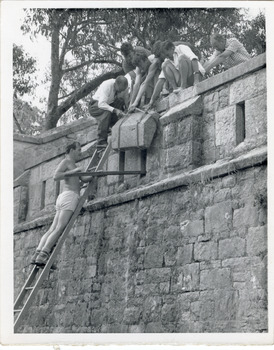 View of outside wall of Powder Magazine Beechworth with a group of workmen at the top and single man poised on a ladder leaning against the wall. 