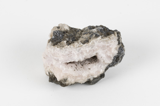 Hand-sized piece of pale pink mineral specimen with dark grey rim and hollowed centre. 