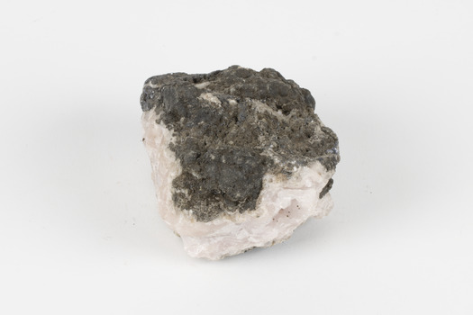 Hand-sized piece of pale pink mineral specimen with dark grey rim and hollowed centre. 
