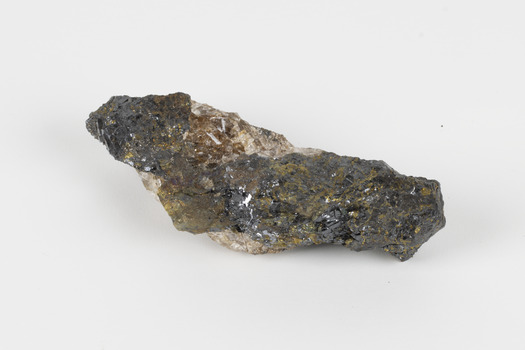 Hand-length specimen of black, brown, gold and beige mineral forming a jagged pipe shape. 