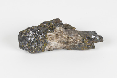Hand-length specimen of black, brown, gold and beige mineral forming a jagged pipe shape. 