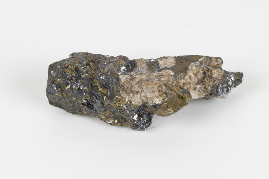 Hand-length specimen of black, brown, gold and beige mineral forming a jagged pipe shape. 