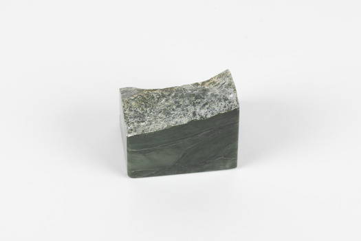 A solid mineral specimen of grey-green stone with pale veins running through it. 