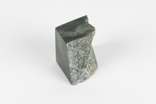 Solid specimen of grey-green rock with some light mottling and veins, two sides are smooth, one is more jagged. 