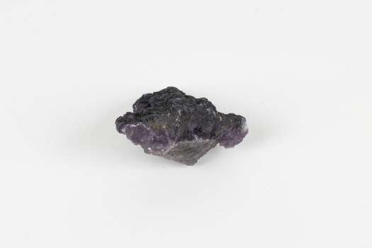 Image shows a medium-sized piece of rough gemstone with a purple interior and dark grey exterior crust. 