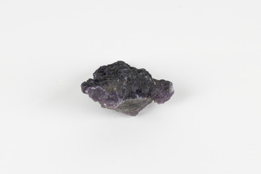 Image shows a medium-sized piece of rough gemstone with a purple interior and dark grey exterior crust. 