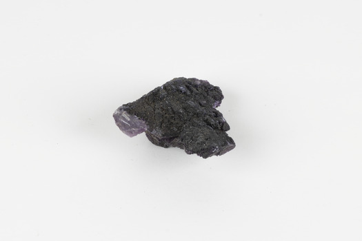 Image shows a medium-sized piece of rough gemstone with a purple interior and dark grey exterior crust. 