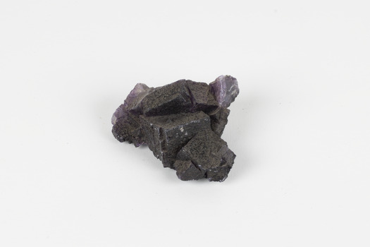 Image shows a medium-sized piece of rough gemstone with a purple interior and dark grey exterior crust. 