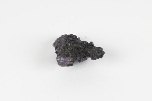 Image shows a medium-sized piece of rough gemstone with a purple interior and dark grey exterior crust. 