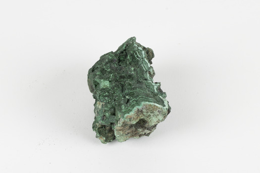 A palm-sized solid mineral specimen with a rough, uneven surface and a variety of green colourations. 