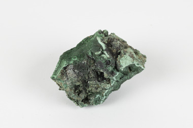 A palm-sized solid mineral specimen with a rough, uneven surface and a variety of green colourations. 