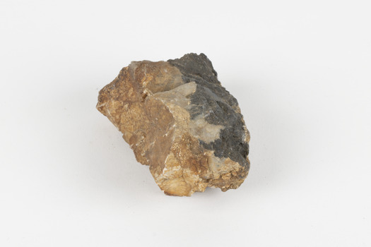 A fist-sized solid geological specimen. Each half is made of a different material, one side is cream and orange/brown coloured, the other side is dark grey
