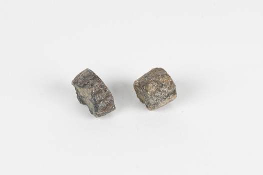 Two pieces of separate mineral specimen in shades of grey, brown, and yellow with crosses in the center