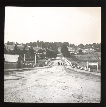 A monochrome photograph within a square frame featuring an image of a street and surrounding landscape