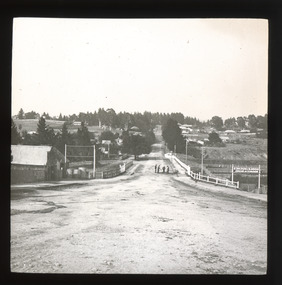 A monochrome photograph within a square frame featuring an image of a street and surrounding landscape