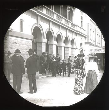 A monochrome photograph within a square frame featuring an image of people walking down the street.