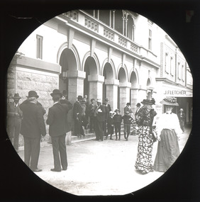A monochrome photograph within a square frame featuring an image of people walking down the street.