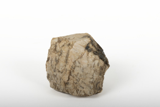 A small textured caramel-coloured rock with brown marbling. Standing upright, slim shape with flat top and bottom. Right side is angled, deep-brown in colour with a glassy texture.
