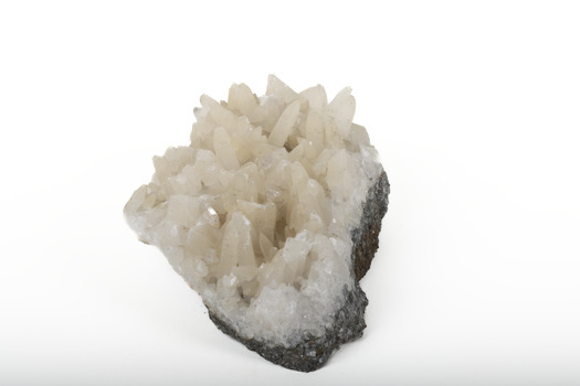 Mineral with a stone coloured base with white crystal like structures erupting from the base in erratic upwards directions.
