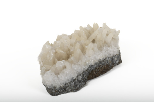 Mineral with a stone coloured base with white crystal like structures erupting from the base in erratic upwards directions.