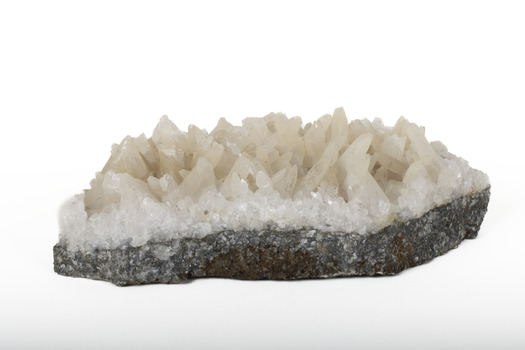 Mineral with a stone coloured base with white crystal like structures erupting from the base in erratic upwards directions.