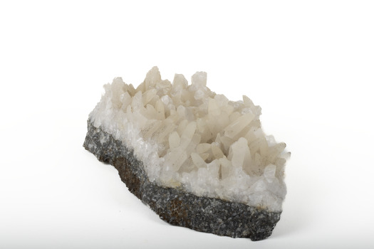 Mineral with a stone coloured base with white crystal like structures erupting from the base in erratic upwards directions.
