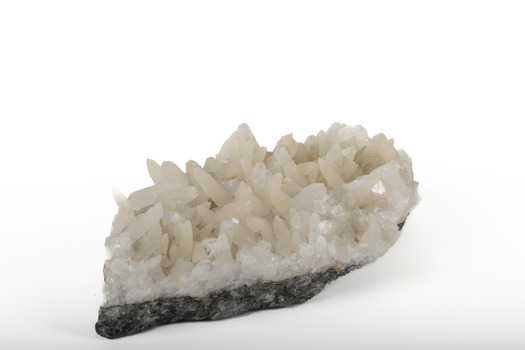 Mineral with a stone coloured base with white crystal like structures erupting from the base in erratic upwards directions.