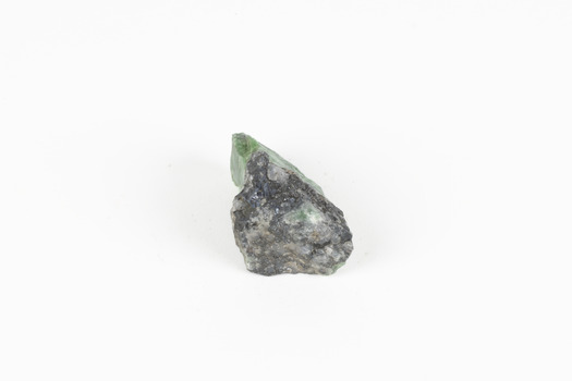 A small solid mineral specimen that is primarily pale green and blue-grey with speckles of beige and white.