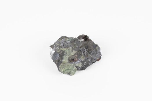 Palm-sized mineral of primarily grey colour, small red gemstones visible, green patches.