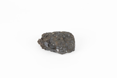 Coin-sized solid mineral specimen in sades of black with black shiny points.