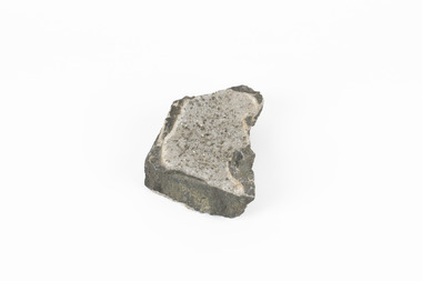 Coin-sized solid mineral with tiny crystals and shades of black and beige.