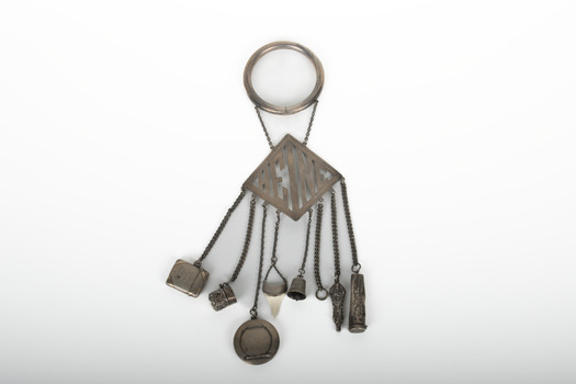 A decorative silver belt hook with small household object attached by chains to a suspended name plate